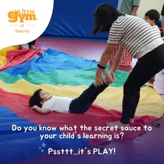 The secret to learning is play. A child enjoys a ride on the colorful parachute, a group activity that builds core strength and teaches cooperation.