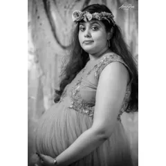 The same studio portrait, presented in classic black and white. This version emphasizes the mother's expression and the soft textures of the gown and floral crown.