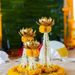 A beautiful and intricate centerpiece combining traditional elements. This arrangement features golden lotus accents rising from a base of fragrant jasmine and marigold flowers, perfect for a pooja or wedding event.
