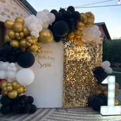 A chic and modern first birthday setup featuring a black, white, and gold color scheme. The gold shimmer wall, custom neon sign, and light-up number '1' create a glamorous photo backdrop for a stylish celebration.