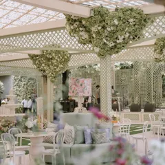 A comfortable and stylish lounge area designed for guests to relax and mingle. The mint green sofa, patterned cushions, and a custom floral lampshade are perfectly framed by heart-shaped floral installations on the trelliswork.