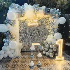 For a chic and modern anniversary party, I designed this stunning photo backdrop. It features a shimmering silver sequin wall, a lush organic balloon arch in silver and white, and a custom neon "Happy Anniversary" sign, all brought together with a light-up number "1" to mark the special milestone.