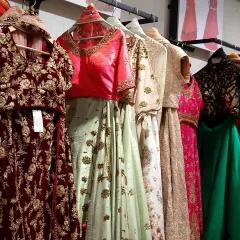 A close-up of some of the outfits available for rent, including a maroon velvet lehenga and a pastel green embroidered set.
