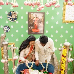 The parents looking lovingly at their daughter in the cradle. The decor includes hanging lotus buds and traditional artwork to create a blessed atmosphere.