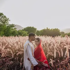 A romantic portrait of a couple in a field of pampas grass, with the hills of Rajasthan in the background. The soft, golden light creates a dreamy and ethereal mood.