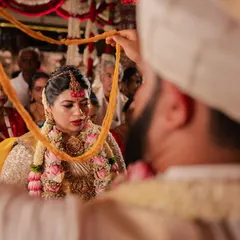 A key moment in a South Indian wedding ceremony, captured from an intimate over-the-shoulder perspective.