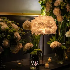 Ambiance is everything. A feather-adorned lamp casts a soft, diffused light over arrangements of white chrysanthemums, creating a moody and textural detail in a lounge corner.