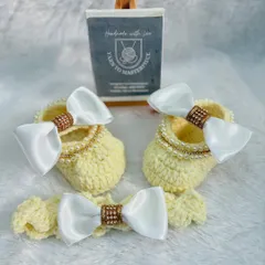 An elegant accessory set in a soft yellow, this includes booties and a headband decorated with large white satin bows that have a sparkly center.