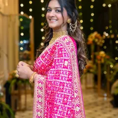 A beautiful, traditional look for a Lagan Lakhvanu ceremony. The bride's bright pink bandhani saree is paired with classic gold jewelry and a soft, glowing makeup look.