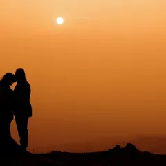 An intimate silhouette of a couple against a warm, orange-hued sunset. This romantic pre-wedding photo focuses entirely on their connection, framed by the evening sky.