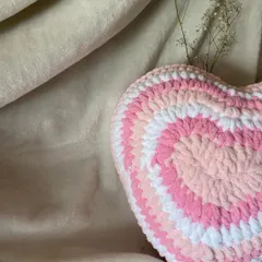 A styled shot of our pink and white crochet heart pillow. The soft, plush texture makes it a perfect decorative accent for a cozy corner of your room.