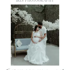 An artistic studio maternity portrait of a couple dressed in all white. The setting features a beautiful backdrop of white blossoms, creating a romantic and serene atmosphere for this pregnancy photo.