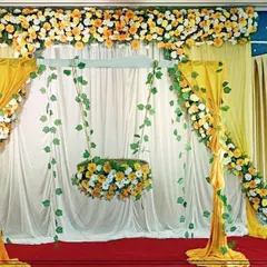 An elegant cradle ceremony decoration featuring a floral swing (jhoola) under a canopy. The yellow and white color scheme with fresh flowers and flowing drapes creates a serene and joyful atmosphere.