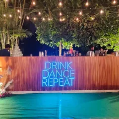 Light up the night with our rustic wooden bar featuring a custom "Drink Dance Repeat" neon sign. This setup is ideal for creating a fun, relaxed vibe at any outdoor party or sangeet.