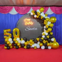 A straight-on view of the 50th birthday decor, showing the balance of black, gold, and white balloons in the semi-arch.