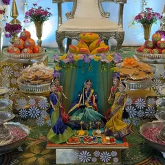 A close-up of a beautiful doll arrangement depicting a Seemantha ceremony. The dolls are surrounded by offering plates filled with traditional sweets and snacks.