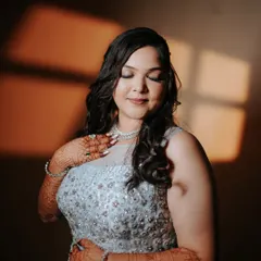 A moment of quiet reflection for the bride. The warm light catches the intricate details of her gown and the beautiful henna on her hands, capturing her glow before the engagement festivities.
