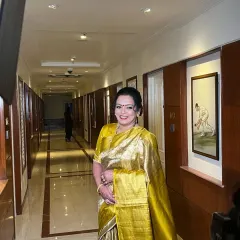 The mother of the groom, looking radiant in a stunning gold saree. Her makeup is classic and elegant, with a traditional red bindi to complete the look.