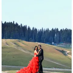 A classic portrait in the meadows of Kashmir. The bride's stunning red gown stands out against the vast green hills and dense pine forest, creating a powerful and romantic image that feels both grand and intimate.