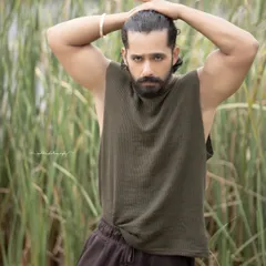 A black and white portrait of an actor in a natural, outdoor setting. The focus is on his strong physique and intense expression, creating a raw and powerful image.