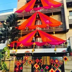 An elaborate house decoration with tent-style draping on each balcony in bright orange and pink fabric. The entrance is adorned with colorful hanging props.