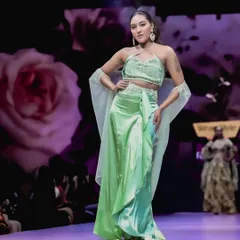 A model strikes a pose in a vibrant green two-piece ensemble. The floral background of the runway screen adds a beautiful, soft contrast to the modern outfit.