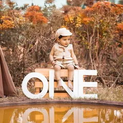 This first birthday portrait captures a thoughtful moment by the water. The natural, earthy tones of the setup and the outdoor location make for a unique and serene milestone photo.