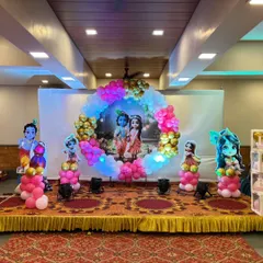 This Radha Krishna themed baby shower stage features a large circular balloon arrangement around a central backdrop, with character cutouts on either side.