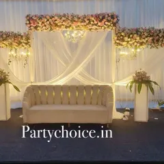 We designed this elegant outdoor reception stage with a clean, white theme. The setup includes a white fabric backdrop with chandeliers, topped with blush pink floral arrangements, creating a dreamy and romantic look.