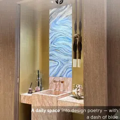 This powder room from 'The Aura House' project was designed to feel like a piece of art. A tall, vertical panel of blue and white agate-style art creates a stunning backsplash, complemented by a pink marble vanity and minimalist pendant lighting.