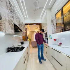 A full view of a recently completed modular kitchen at ATS Nobility. The design features marble-patterned upper cabinets, sleek white lower cabinets, and integrated profile lighting in the ceiling for a clean, modern aesthetic.