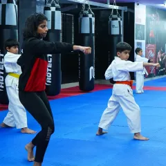 A coach demonstrates the correct form for a punch, with a young student mirroring the movement. This one on one attention is key to developing proper karate technique and muscle memory.