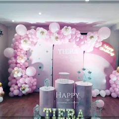 A dreamy pink-themed decoration for a baby girl's first birthday or baby shower. The setup includes a large balloon arch, custom backdrops, and pedestals for the cake.