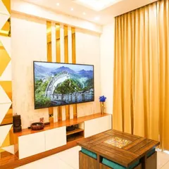 A vibrant and modern living room featuring a custom TV unit with a geometric gold-mirrored partition. The combination of wood, white laminate, and metallic accents creates a lively and stylish entertainment area.