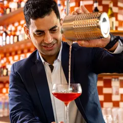 He’s not just behind the bar, he’s behind the brilliance of every pour. Say hello to Varun, our award-winning mixologist, as he crafts a vibrant red cocktail.