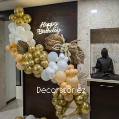 For a more sophisticated celebration, I design trendy boho-themed decor. This setup combines an organic cascade of chrome gold, white, and nude balloons with dried pampas grass and palm spears, all highlighted by a warm neon birthday sign.
