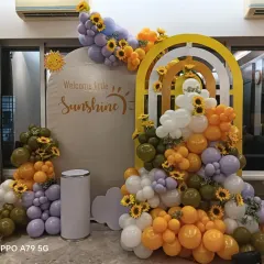 A "Welcome Little Sunshine" theme with a cheerful and unique color palette. The mix of olive green, lavender, and orange balloons, accented with sunflowers, creates a bright and happy setting.