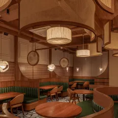 For the Eat Punjab restaurant in Gandhinagar, we designed an immersive dining experience using warm, natural materials. The space is defined by curved, upholstered booth seating in deep green, complemented by custom cane and wood ceiling installations and drum pendants that cast a soft, inviting glow.