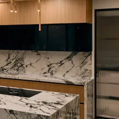 The kitchen island is wrapped entirely in dramatic black and white marble, making it a true statement piece. The modern gold light fixture above adds a touch of elegance.