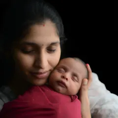 A mother's gentle touch and a sleeping newborn. This close-up, artistically lit portrait is incredibly serene and captures the deep, peaceful love between a mom and her new baby.