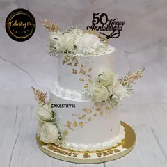 We created this elegant two-tier pineapple cake to honor a beautiful fifty-year love story. It features pristine white frosting, delicate gold leaf accents, and arrangements of fresh white roses, all coming together for a timeless 50th-anniversary centerpiece.