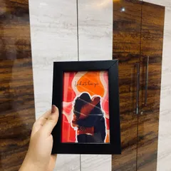 A still image of the pop out couple frame, held against a wooden background. This shot clearly shows the 3D effect and the vibrant colors of the illustration.