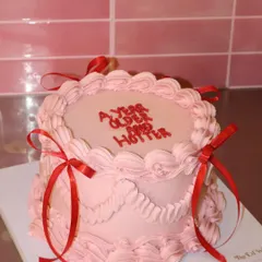 A year older and a year hotter. This pretty pink cake features sassy text, delicate piping, and bright red ribbons for a fun and confident birthday statement.