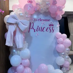 An elegant 'Welcome Princess' decoration for a baby girl's arrival. This home setup features a white arched backdrop, a pink and white balloon arch, and a large fabric bow for a delicate touch.
