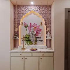 A beautifully designed mandir featuring a custom backdrop with a lotus mural and intricate wallpaper. The space is illuminated by hanging brass bells and includes a marble-topped cabinet for storage, creating a perfect blend of devotion and design.