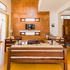 The living room in Anand and Madhu's home features a stunning rammed earth wall as the backdrop. The space is designed to be warm and inviting, with custom wooden furniture and large openings to the outside.