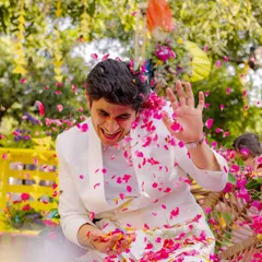 The groom gets his turn! A candid shot of the groom laughing as he is showered with pink flower petals during a fun and energetic Haldi celebration.