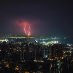A dramatic drone photograph capturing a powerful red lightning strike over the Mumbai coastline and the Trans Harbour Link at night.