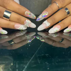 An ethereal and intricate design featuring 3D sculpted flowers, rhinestone bows, and iridescent diamond-shaped gems on long almond nails.