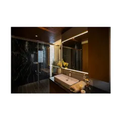 The master bathroom features a dark and moody palette, with black marble walls and a wood-paneled ceiling. The clean lines of the vanity and the backlit mirror create a sophisticated and spa-like atmosphere.
